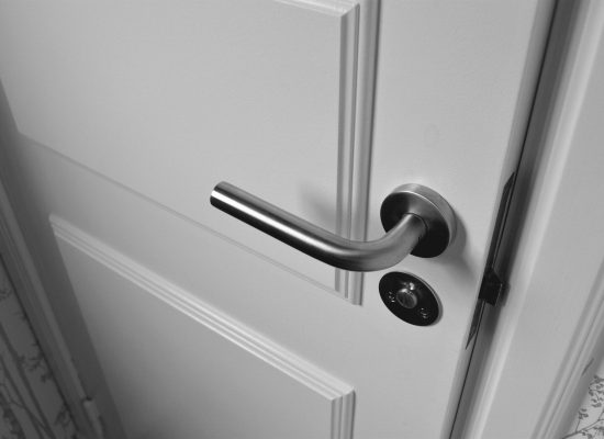 Close-up of a sleek steel door handle on a white door, showcasing modern interior design in monochrome.